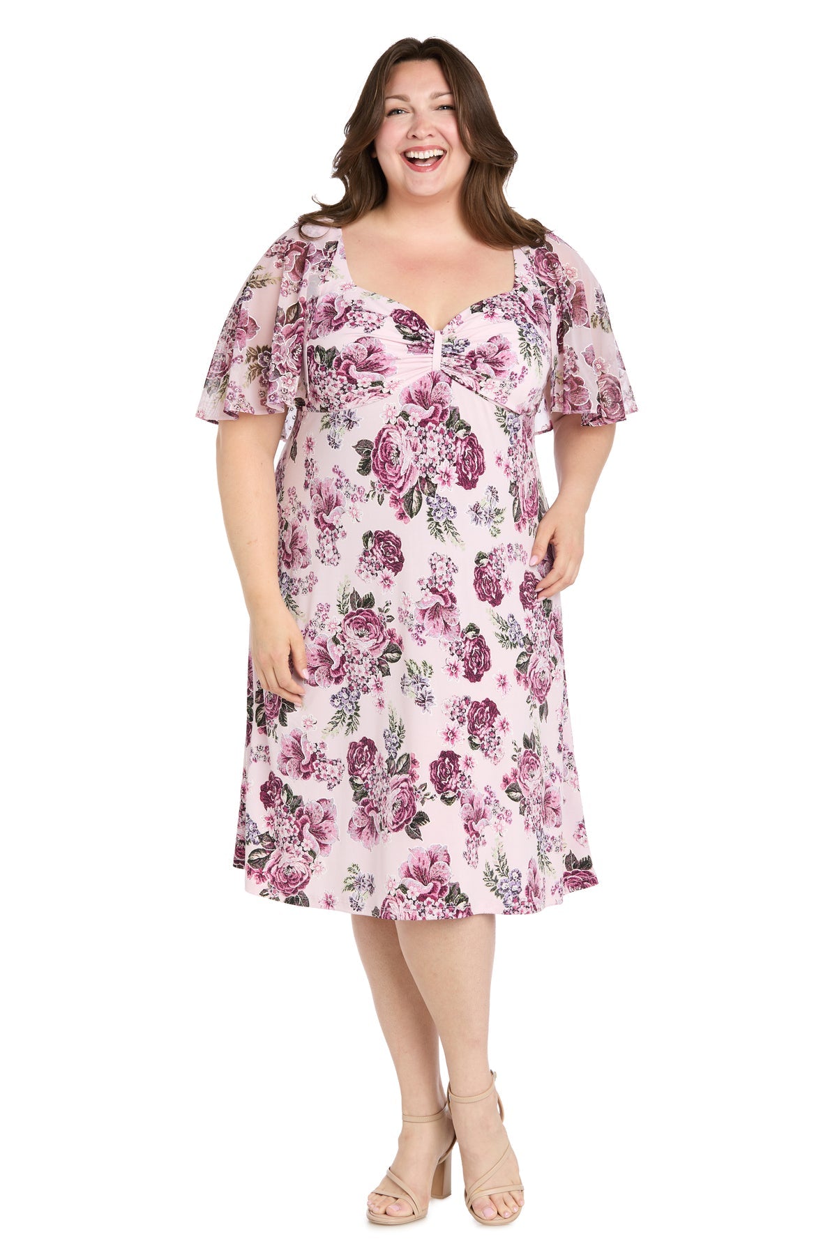 Woman wearing the Plus-Size Pink Party Dress: R&M Richards 3467W, a knee-length light pink cocktail dress with flutter sleeves and beige heels, smiling against a white background.